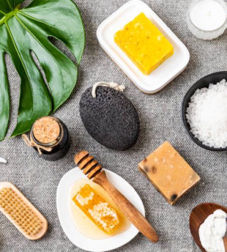 Top view of various skin a body care products such as a bath sponge, a candle, a brush, handmade soaps, honey, a pumice stone, salt, a towel, and a white bottle. Predominant colors are grey, yellow and beige. Studio shot taken with Canon EOS 6D Mark II and Canon EF 24-105 mm f/4L